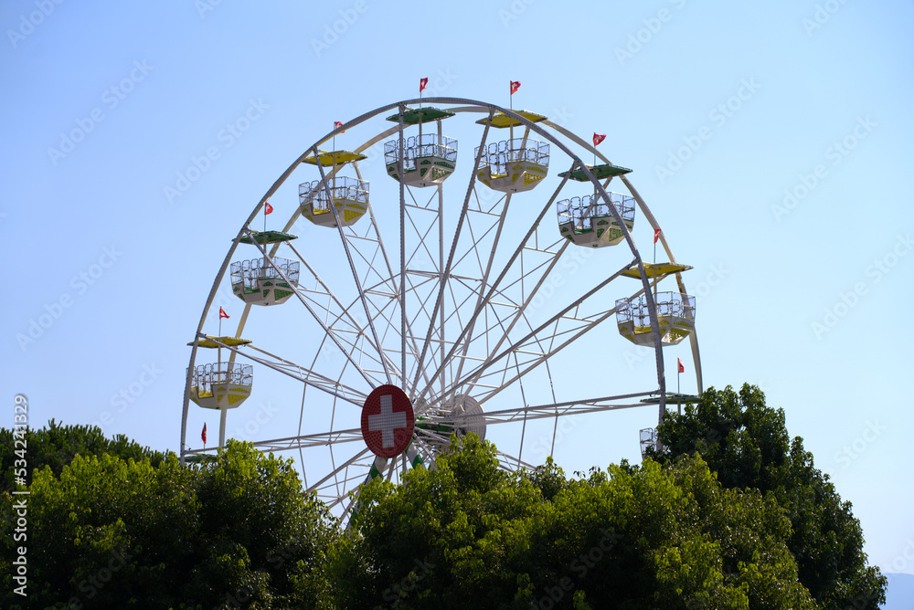 Ferris wheel with Swiss flag at village of Ascona, Canton Ticino, on a sunny summer day. Photo taken July 24th, 2022, Ascona, Switzerland.