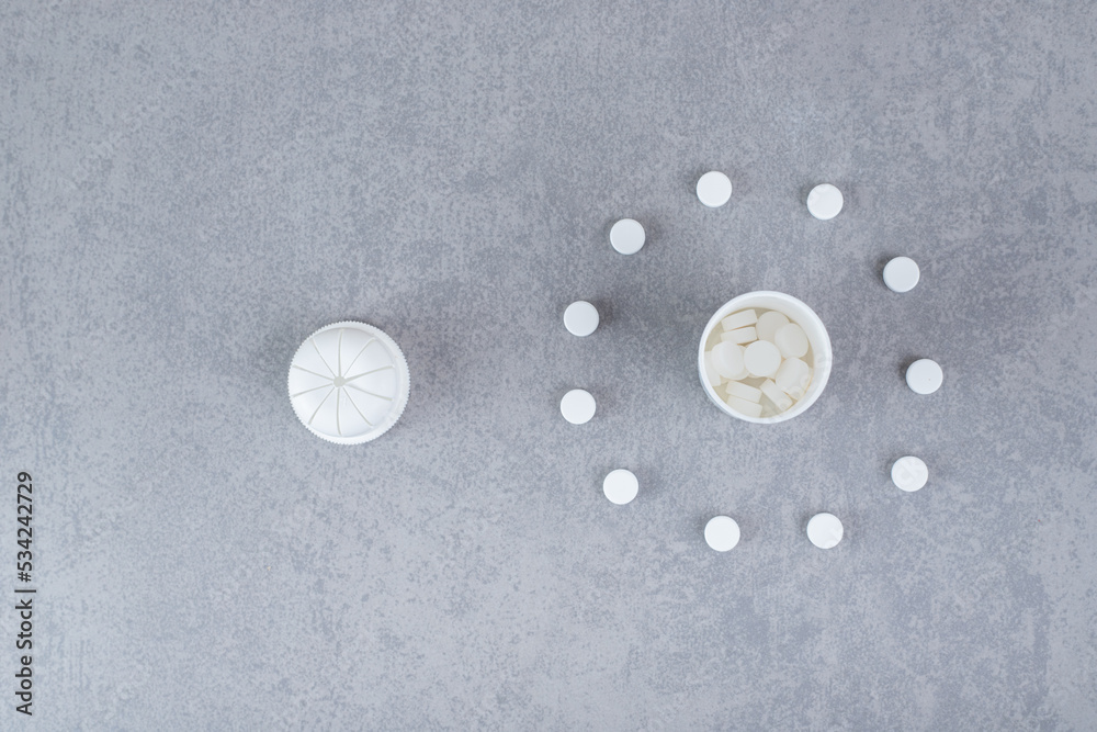 A small white jar of white pills on gray background A small white jar of white pills on gray background