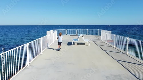 Boy riding scooter on a pier at sunyday photo