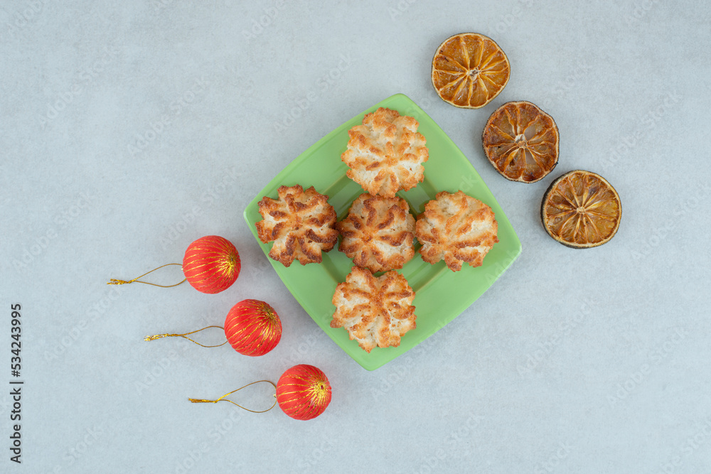 A green plate of round sweet cookies with dried oranges and Christmas balls A green plate of round sweet cookies with dried oranges and Christmas balls
