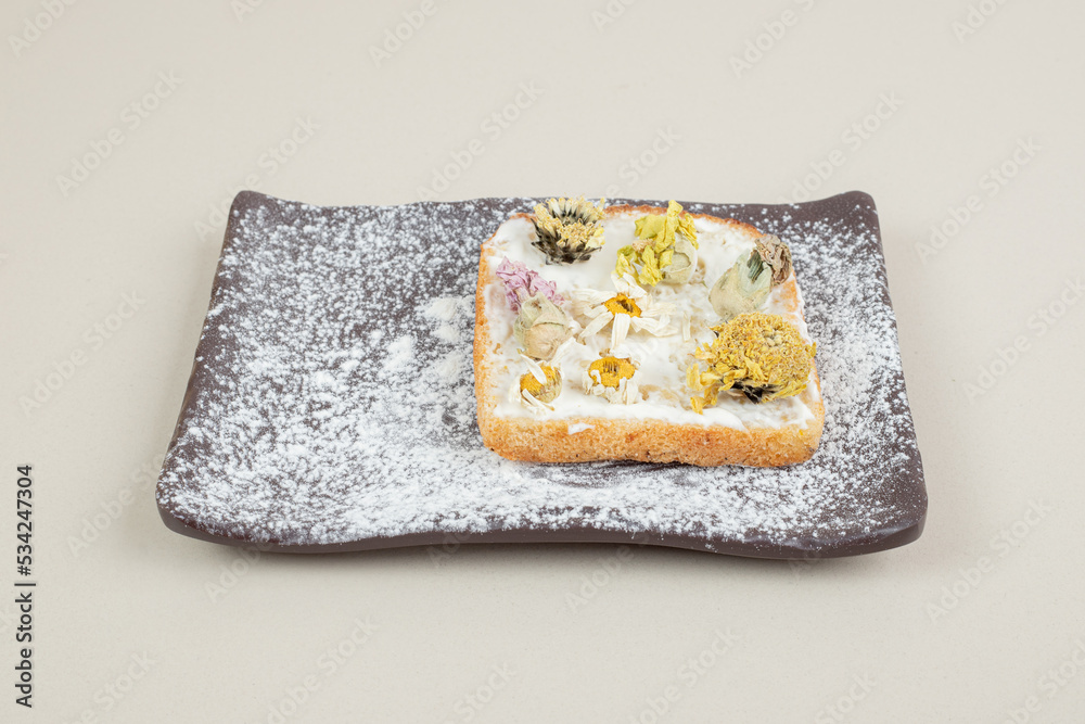 Toast with dried flowers and flour on dark cutting board