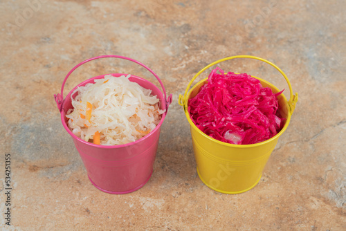 Two buckets of red and white sauerkraut on marble surface