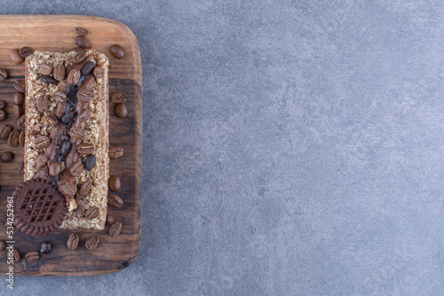 Wooden board under a slice of cake with biscuit and coffee beans on marble background