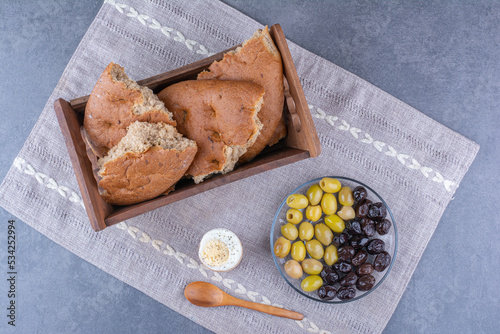 Breakfast setup of bread tray, soft-boiled egg and a platter of pitless olives on a small tablecloth on marble background photo