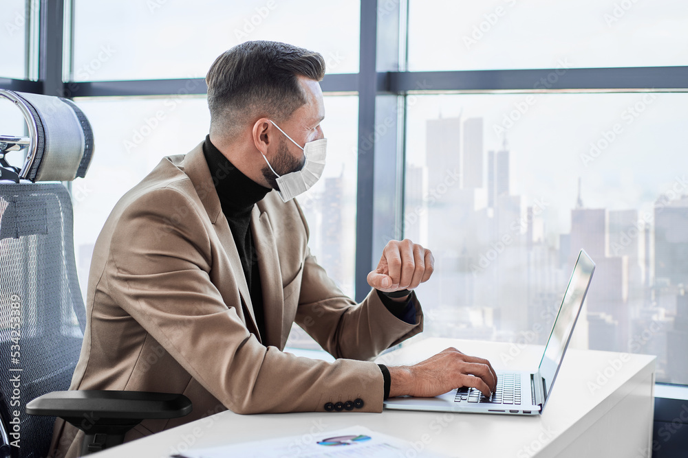 businessman in a protective mask working on a laptop in the office. businessman in a protective mask working on a laptop in the office.