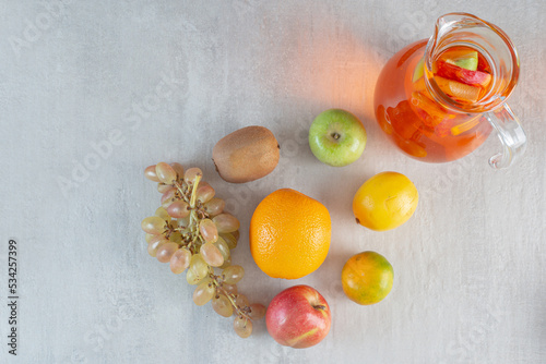 A glass jug of juice with fruits on marble background