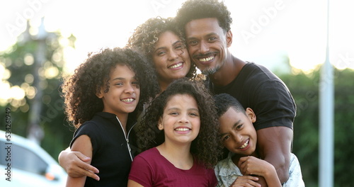 African family mixed race parents and children hugging together outside in sunlight