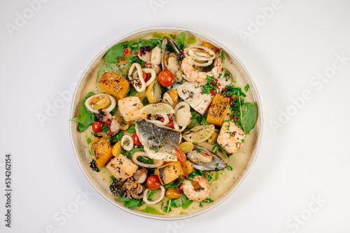 Dish of boiled dorada fish with shellfish, vegetables and herbs
