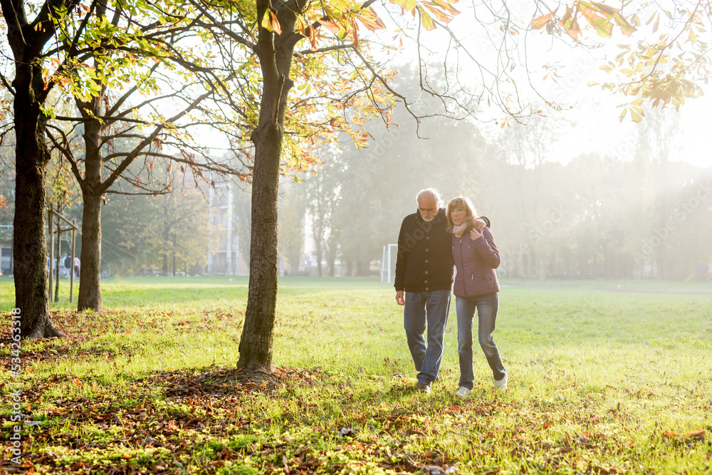 Senior married couple walking together hugging outdoors in autumn countryside