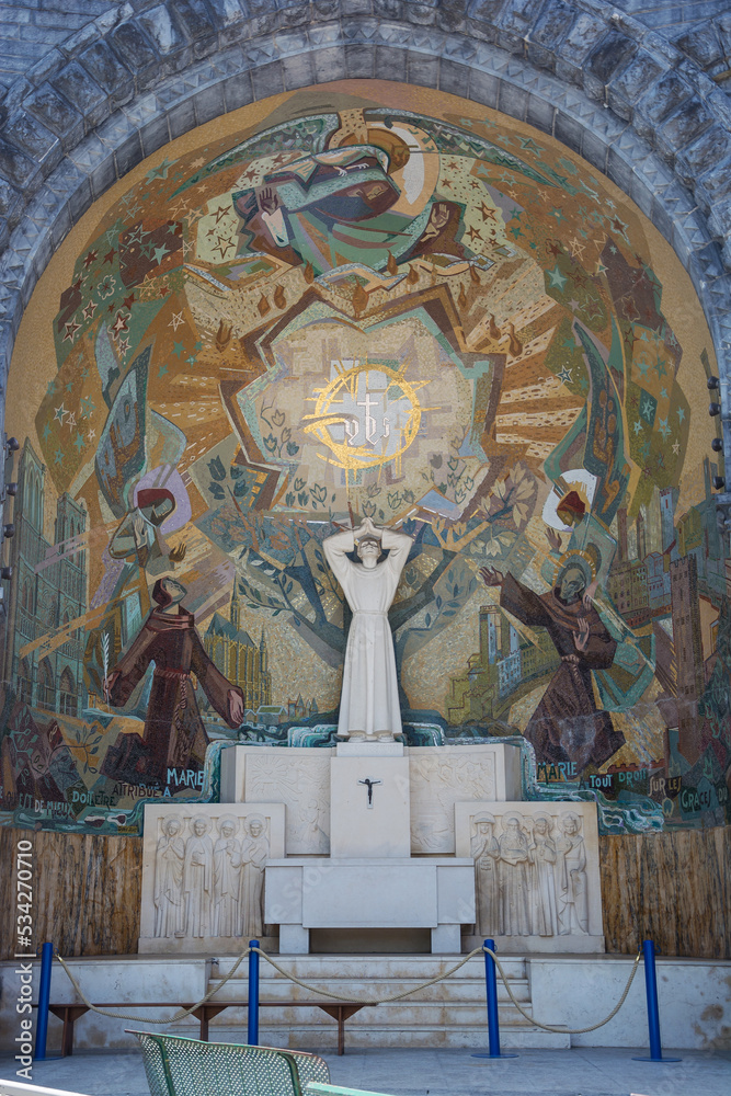 Statue and frescoes in the niche near the Basilica of the Holy Rosary in Lourdes, France