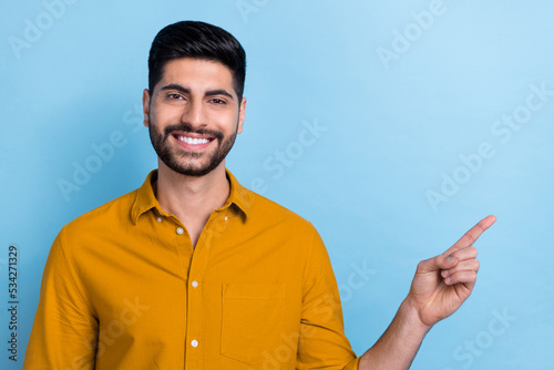 Photo of cheerful positive beaming toothy man wear yellow shirt smiling indicating at empty space isolated on blue color background