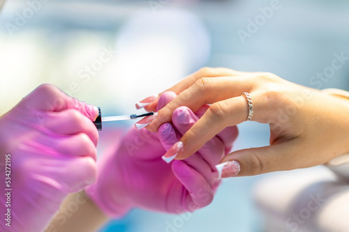 On the nail of a young girl or woman, manicure master - a manicurist applies a transparent varnish in a beauty salon. Nail care during manicure procedure.