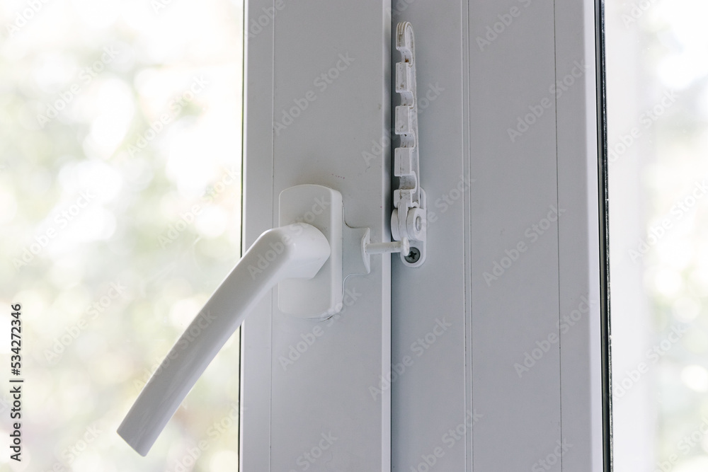 Close-up of a white pvc balcony door handle, an insulating glass window comb fixes the sash. Fittings for child protection and safe ventilation
