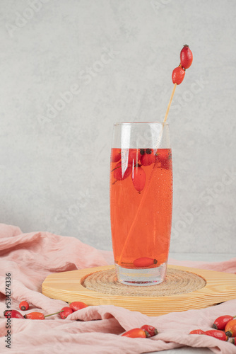 Glass of fresh lemonade with rosehips on wooden plate