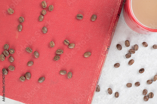 Red cup, coffee beans and book on marble background
