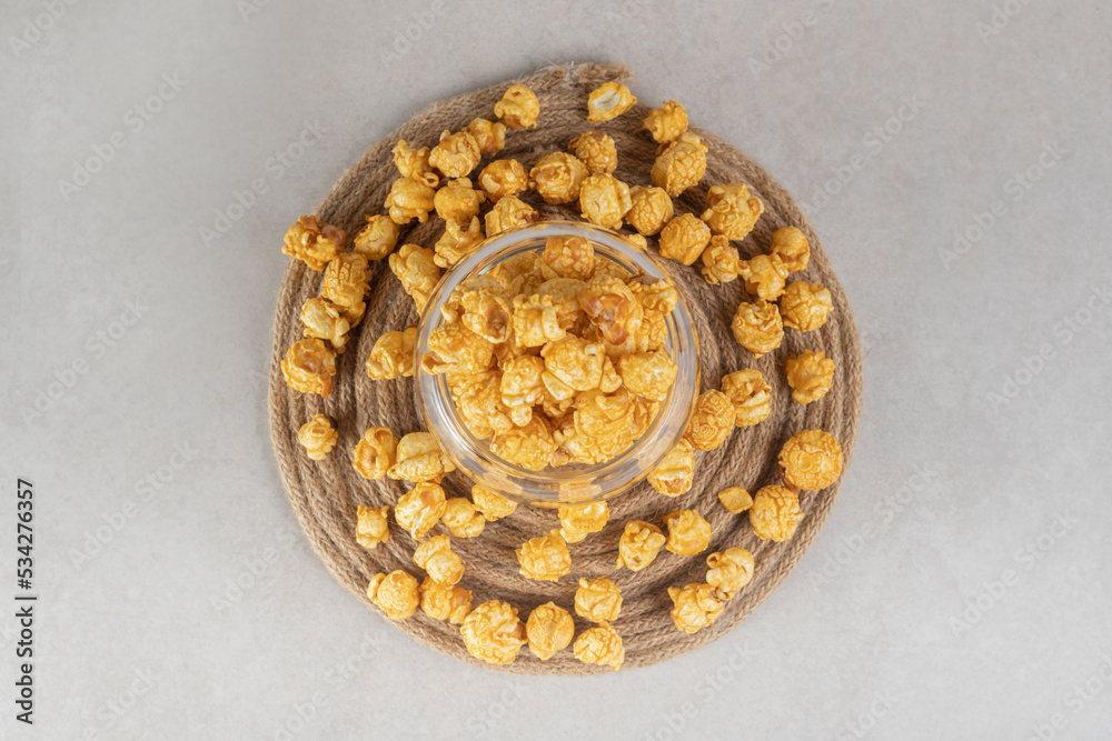 Glass bowl placed on a knitted trivet, filled and encircled with caramel coated popcorn on marble background Glass bowl placed on a knitted trivet, filled and encircled with caramel coated popcorn on marble background