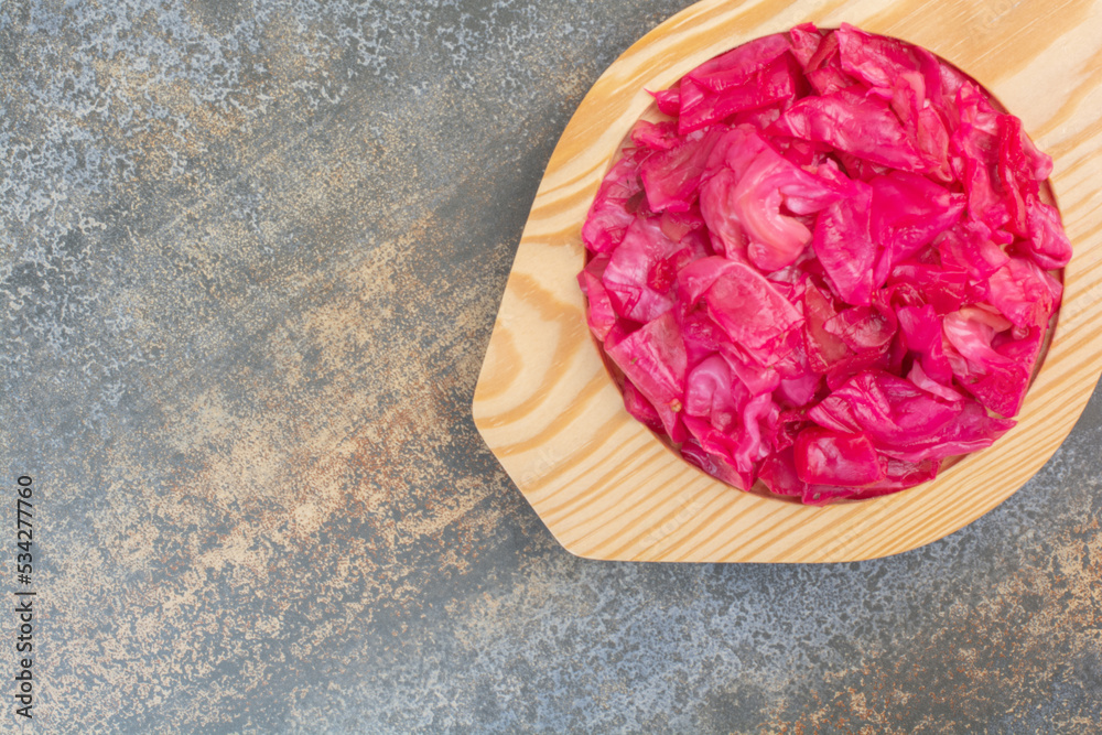 A wooden plate full of red salty cabbage on marble background A wooden plate full of red salty cabbage on marble background
