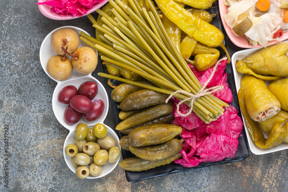 A dark plate full of pickled cucumbers and red salty cabbage on marble background