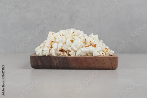 Small wooden tray with a serving of freshly cooked popcorn on marble background