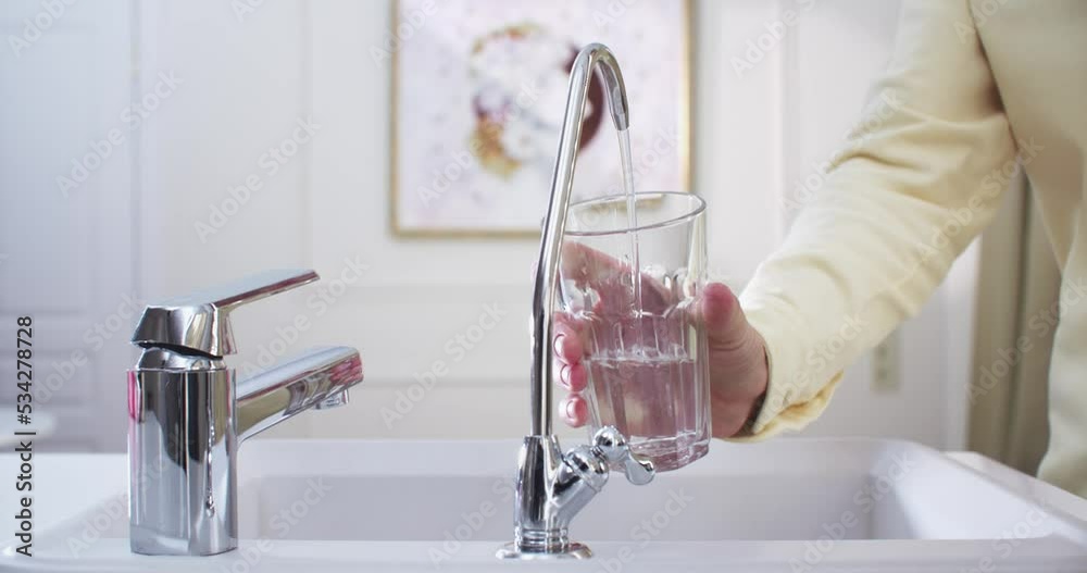 Woman’s hands in the kitchen draw filtered water from a filter faucet into a glass. The filter faucet is in the center, medium shot. 4K