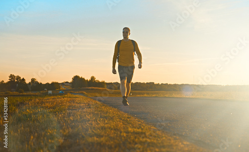 Man with backpack walks along the road on the sunset.