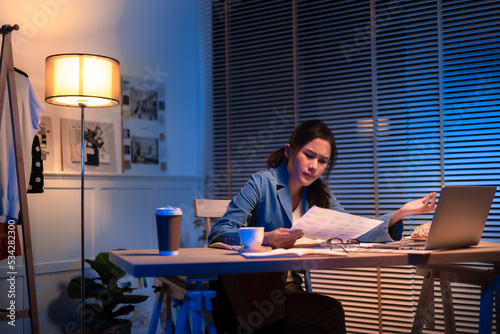 Entrepreneur using tablet pc while working from dark office working on deadline. Business asian woman working overtime at home.