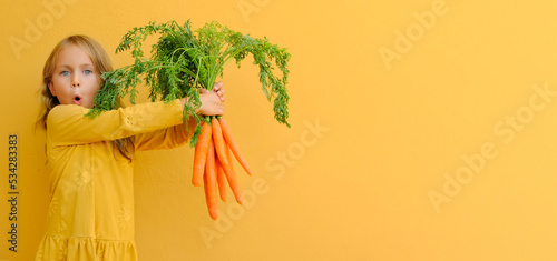 Yellow bright. Excited child girl holds big bunch of carrots isolated orange background. Healthy food and vegetarianism. vitamins mineral healthy mock up banner photo