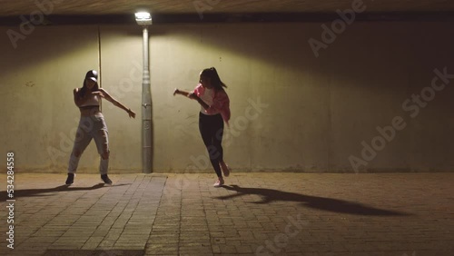 Hip hop, night and girl dance group on a city street dancing under a light in freedom performance, teamwork and action. Friends, dancers and creative women with urban, energy and artistic movement