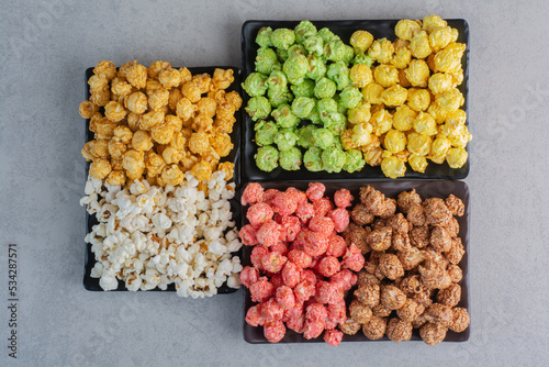 Plates of different colored popcorn candies and simple popcorn on marble background