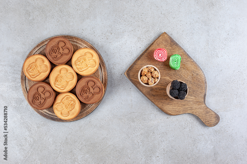 Decorated cookies on wooden board next to glazed peanuts, mullberries and marmelades on marble background Decorated cookies on wooden board next to glazed peanuts, mullberries and marmelades on marble background