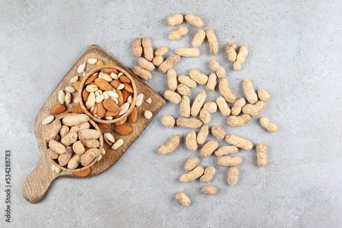 Assortment of nuts in bowls on wooden board and scattered on marble background