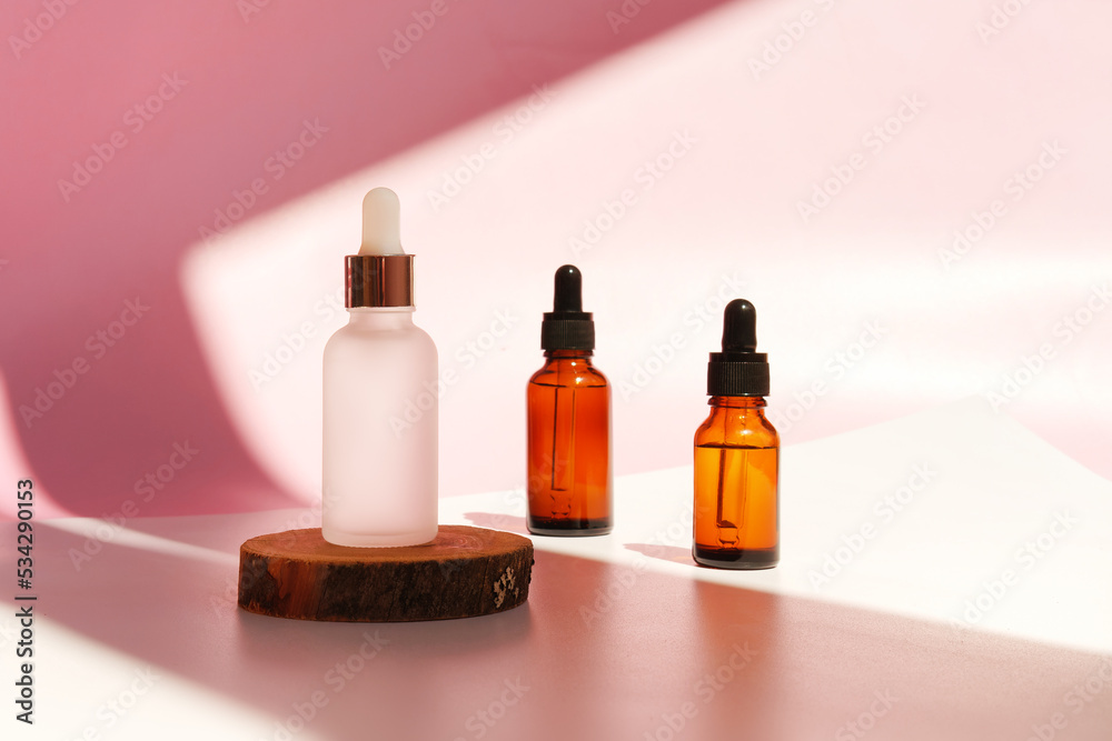 Banner of three transparent amber and frozen glass dropper bottles on pink background in the sunlight. Wooden podium. Pipette with fluid hyaluronic acid, serum, retinol. Cosmetics, healthcare, beauty Banner of three transparent amber and frozen glass dropper bottles on pink background in the sunlight. Wooden podium. Pipette with fluid hyaluronic acid, serum, retinol. Cosmetics, healthcare, beauty