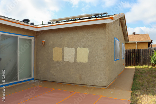 The outside of a house with masking paper and tape prepared for painting. Wall with paint swatches.