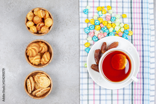 Bowls of cookies and tea with dates and candies on marble background