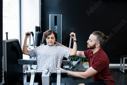 Older woman working out on the machines at the gym with her personal trainer