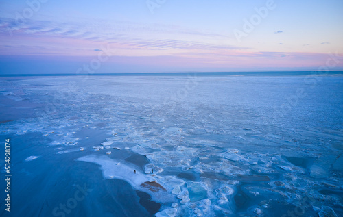 Aerial view of sunset over the frozen sea. Winter landscape on seashore during dusk. View from above of melting ice in ocean on sunrise with horizon. Global warming. Vivid colorful skyline scenics. © artiemedvedev