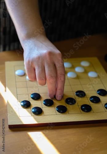 Hands of woman playing Asian board game. Chinese go game board, close up view of playing black and white stone pieces