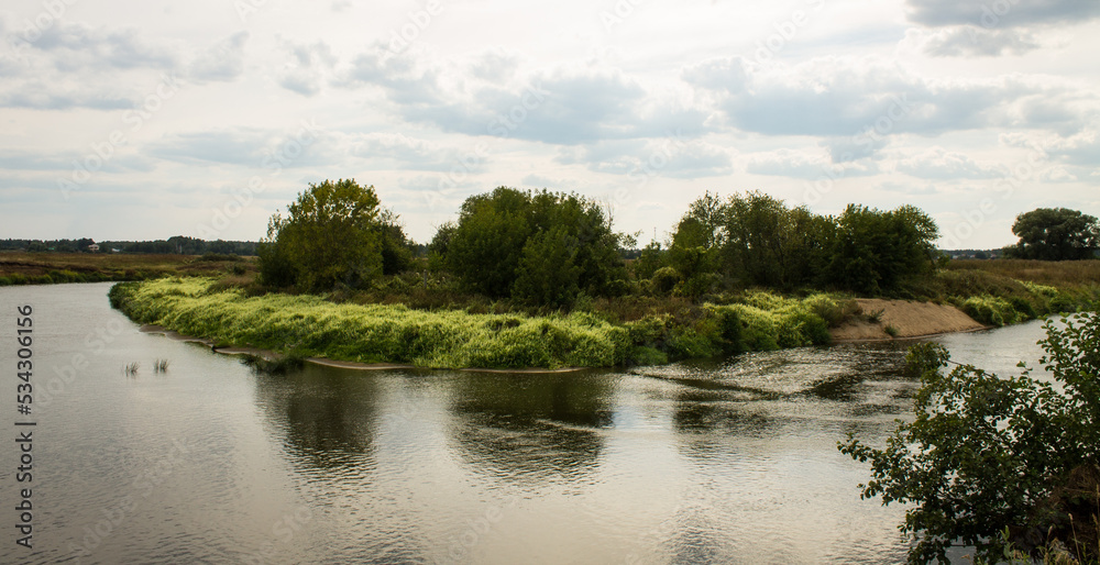 Beautiful landscape - the Klyazma river between the banks with green grass and trees against a cloudy sky on a summer day in the Moscow region and copy space