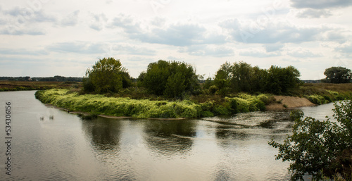 Beautiful landscape - the Klyazma river between the banks with green grass and trees against a cloudy sky on a summer day in the Moscow region and copy space