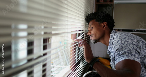Black man looking through kitchen blinders looking outside photo