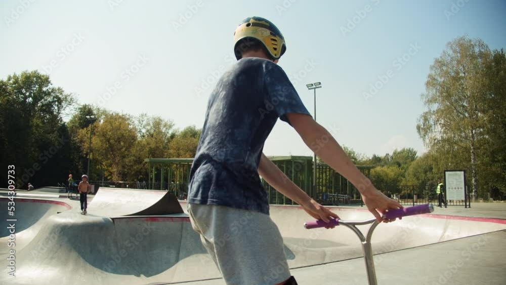 Man making trick on kick scooter in concrete bowl, air extreme in skate park, grab and barspin jump, young skater boy. 