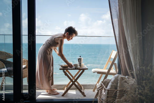 A young woman prepares breakfast on the terrace of her house or hotel in summer. Rest by the sea.