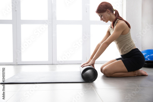Sexy beautiful sportswoman girl unrolls a fitness mat. Place for text. Yoga. Gymnastics