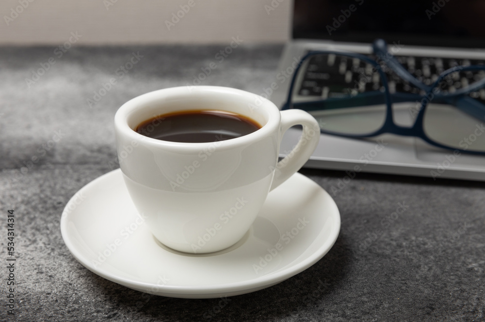 Top view of the office desk. Workspace with laptop, glasses and coffee cup on textural black background.Flat lay. Top view of the office desk. Workspace with laptop, glasses and coffee cup on textural black background.Flat lay.