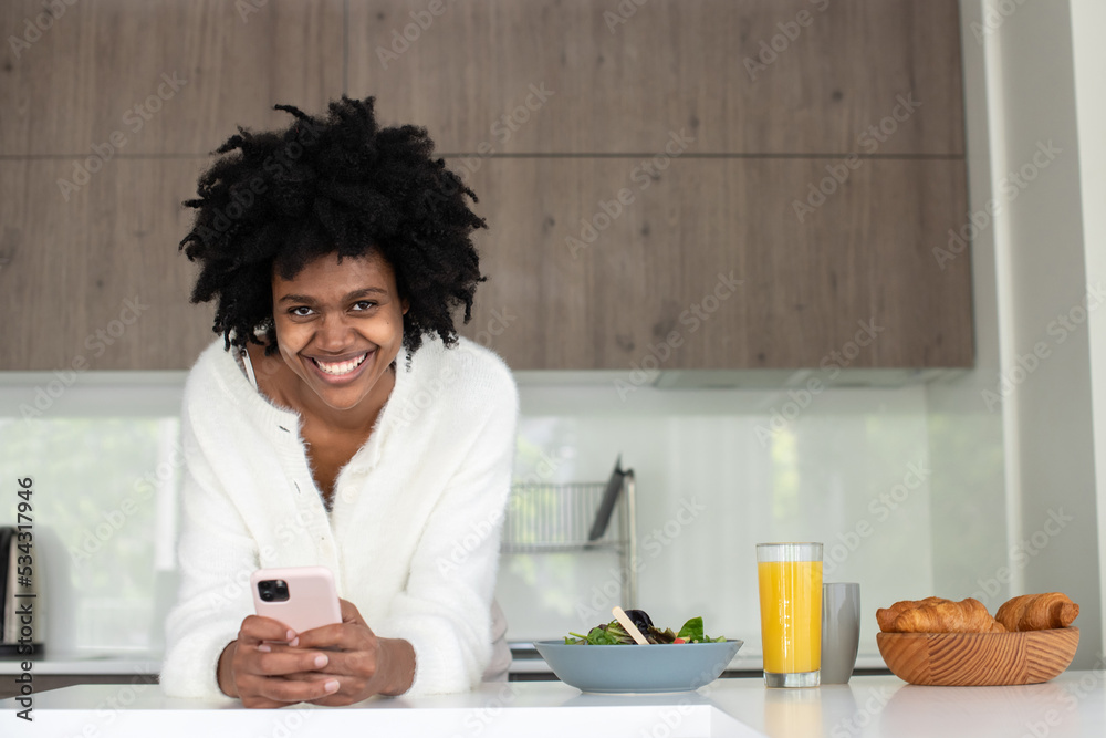 Portrait of young woman working from home typing and smiling. Happy female model leaning on kitchen table, looking at camera. Portrait, remote work concept Portrait of young woman working from home typing and smiling. Happy female model leaning on kitchen table, looking at camera. Portrait, remote work concept