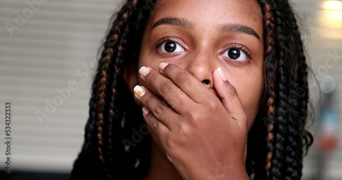Child shocking reaction to news, black ethnicity girl suprised covering mouth with hand
