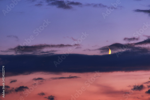 Blue hour with the moon and clouds in the red blue sky. Moon obscured by clouds in the evening light.