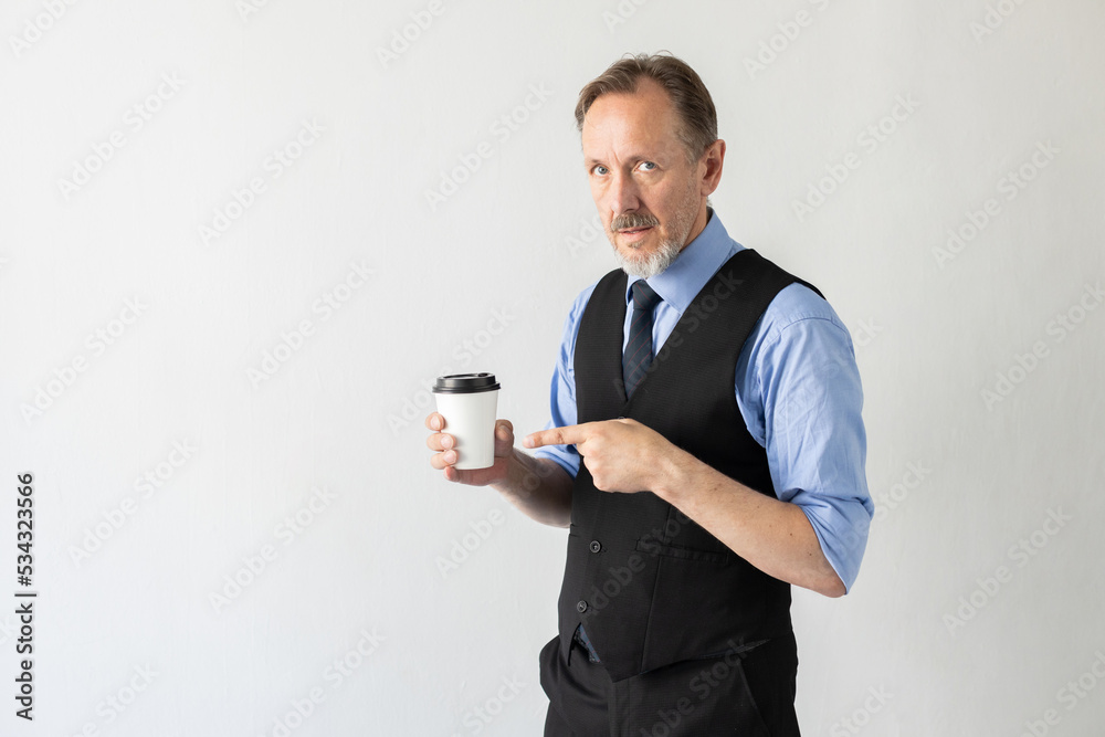Portrait of confident mature businessman pointing at coffee. Senior Caucasian manager wearing formalwear looking at camera and advertising takeout drink against white background. Coffee break concept Portrait of confident mature businessman pointing at coffee. Senior Caucasian manager wearing formalwear looking at camera and advertising takeout drink against white background. Coffee break concept