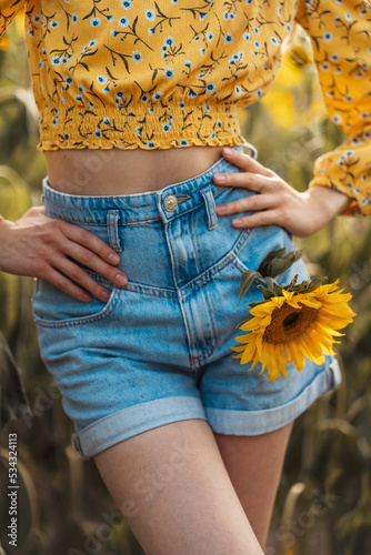 Girl in denim shorts. A sunflower in her pocket. Beginning of autumn. Summer. Concept. Fashion and beauty.