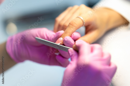 The nail of a young girl or woman in selective focus is cut with a nail file by a manicurist  a manicurist in a beauty salon. Nail care during manicure procedure.